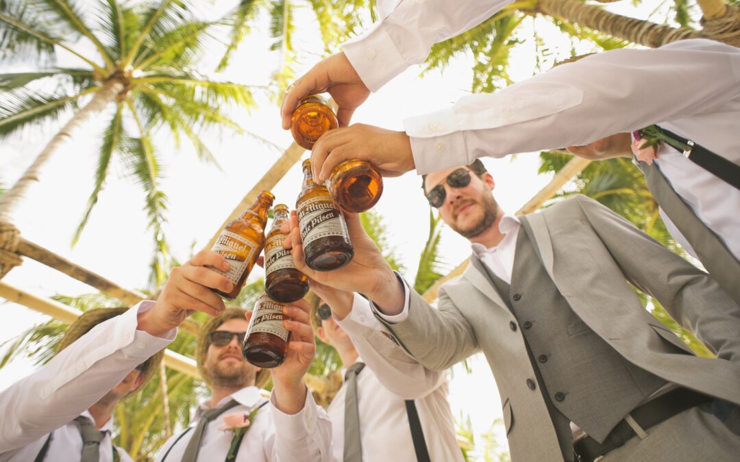 Men at wedding cheers-ing with beers under palm trees